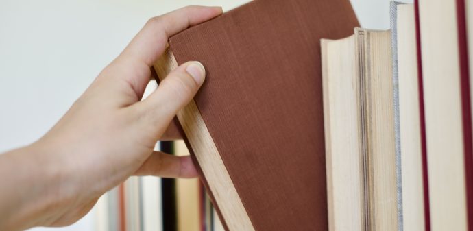 Hand reaching out to select book from library book shelf